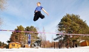 Praticante saltando sobre uma fita de slackline em uma paisagem com neve.