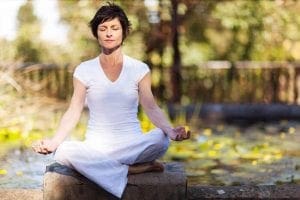 Mulher meditando sentada com as pernas cruzadas em um ambiente arborizado.